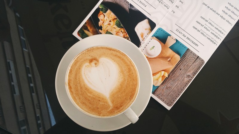 latte in a white cup and saucer on top of a recipe card on a glass table, coffee and recipe on a table 4k