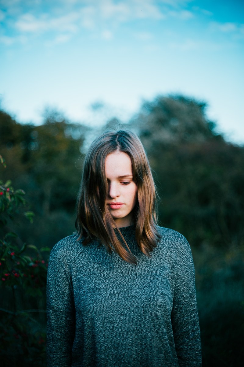 a young woman wearing a sweater is looking down with trees in the background, _inbetween 4k