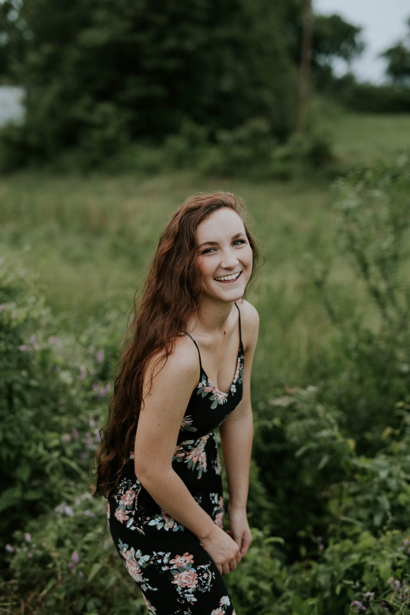 a long haired woman in a black floral dress laughs in a green field, laughing woman in floral dress 4k