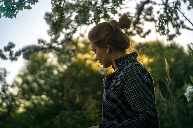 a woman with a bun wearing a coat looks down against a background of trees, woman in a bun looking down 4k