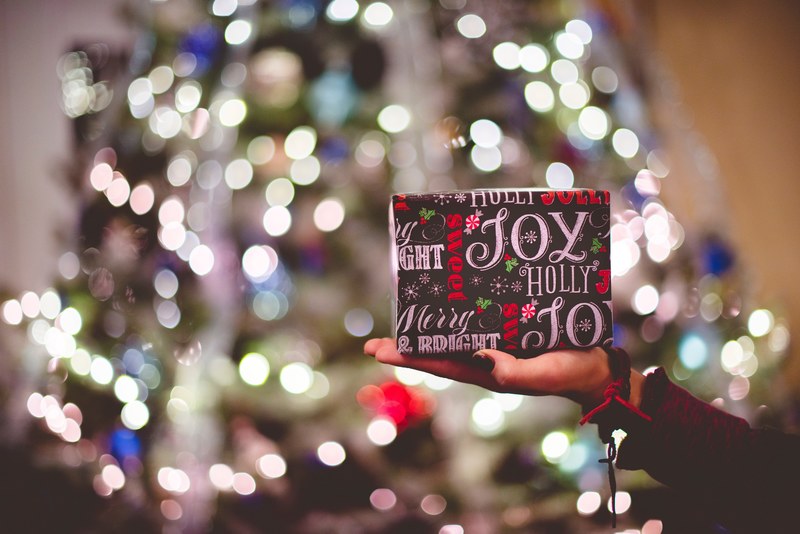 hand held a christmas present wrapped in holiday paper by a tree, christmastime traditions 4k
