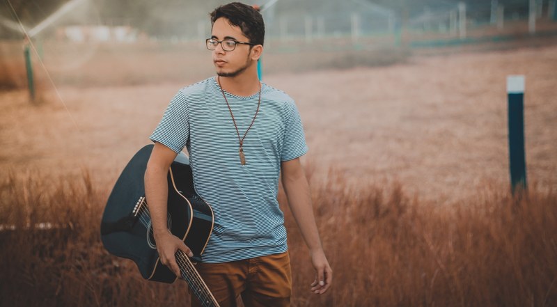a man in a striped shirt with glasses is holding a guitar in a field, _man holding a guitar 4k