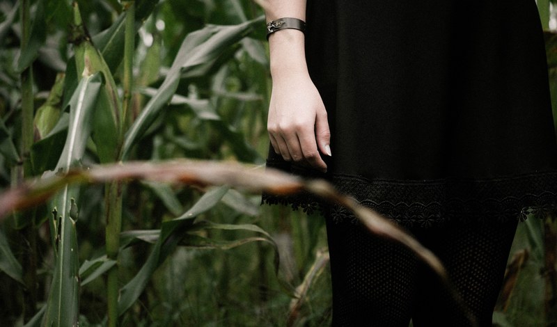 a low shot of a woman dressed in black standing in a green field, lady in black in a field 4k