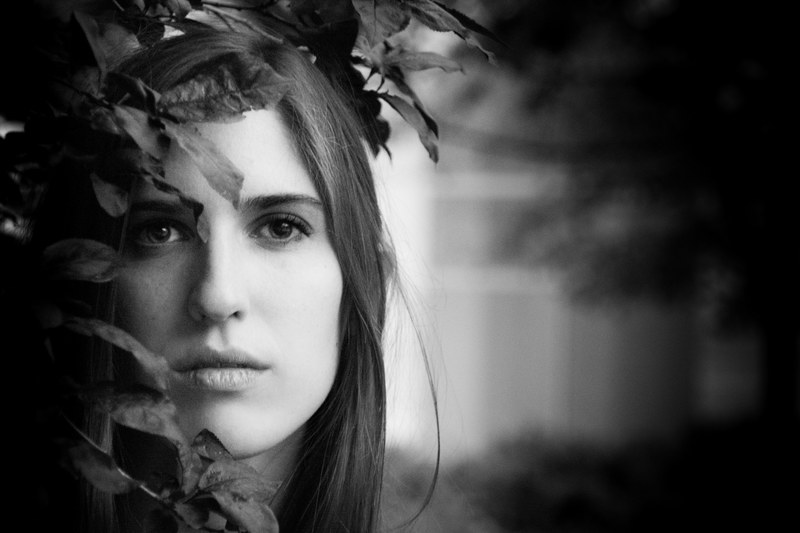 black and white portrait shot of attractive dark haired womans head amongst leaves, monochrome woman in leaves 4k