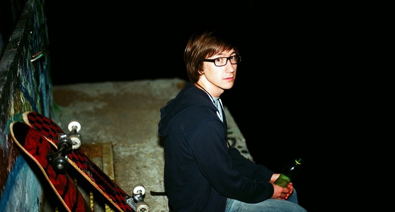 man holding a bottle sitting on a skate ramp by skateboards, skater boy 4k