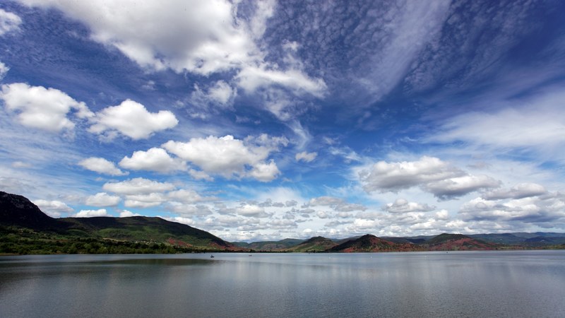 a scenic landscape photo of a lake with patchwork hills on the horizon and fluffy clouds above, peaceful lake 4k