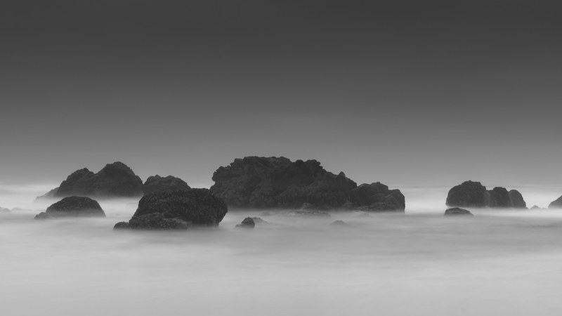 a black and white shot of large rocks jutting out from the frothy sea, black and white rocks in the sea 4k