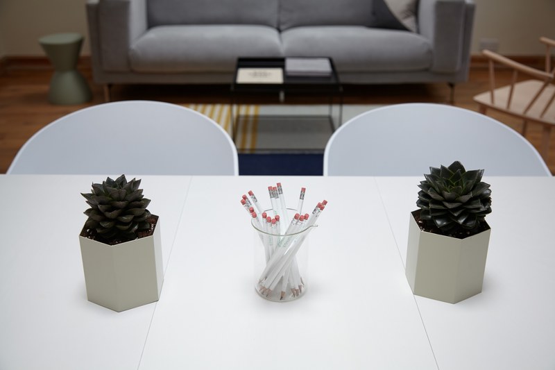 a cup full of pencils and two small potted plants on a white table in an office, chairs sofa plants pencils 4k