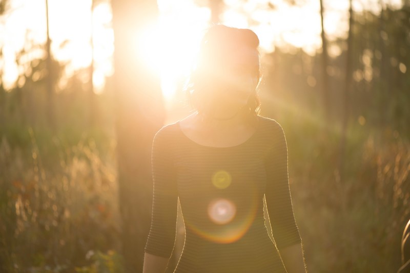 a woman in a striped blouse with bright sun behind her back in a forest, woman in blinding sun 4k