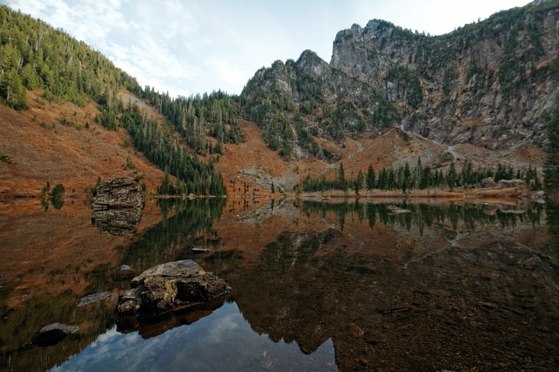a wooded cliff reflected in heather lake, cliff over a clear lake 4k