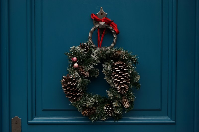 an evergreen wreath decorated with berries and pine cones hangs on a teal door, december means christmas 4k