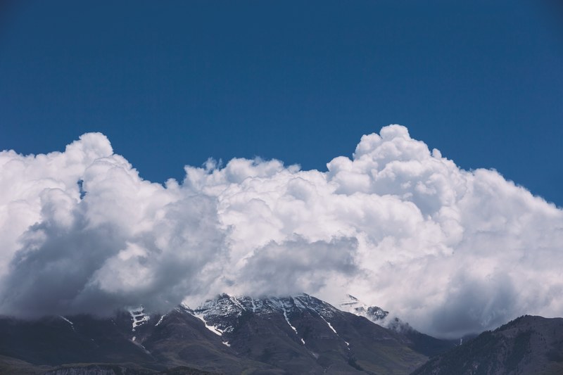a massive white cloud over a snow capped mountain ridge, heavy cloud over mountains 4k