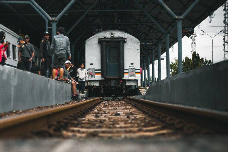 diverse group of people wait for the train to arrive at the platform, station purwokerto 4k