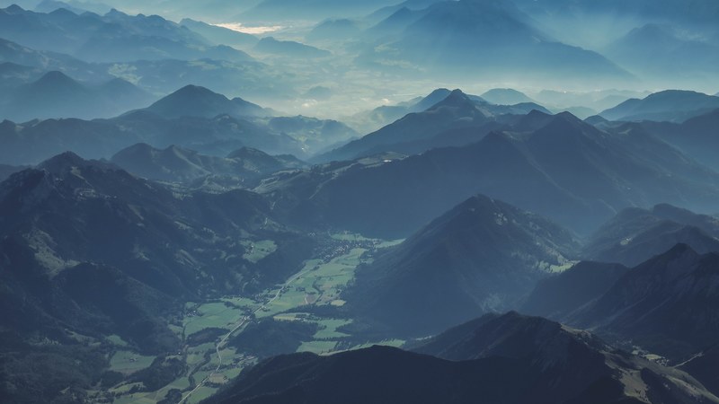 an aerial shot of an alpine landscape with a green valley surrounded by mountain ridges, alpine valley 4k
