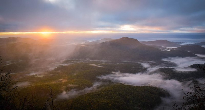 a high shot of mist over wooded mountain slopes during sunset, sunset over whiteside mountain 4k