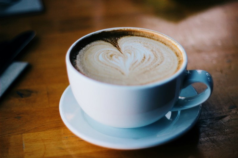 macro of white cup and saucer with latte foam art on wooden table, macro latte foam artwork 4k