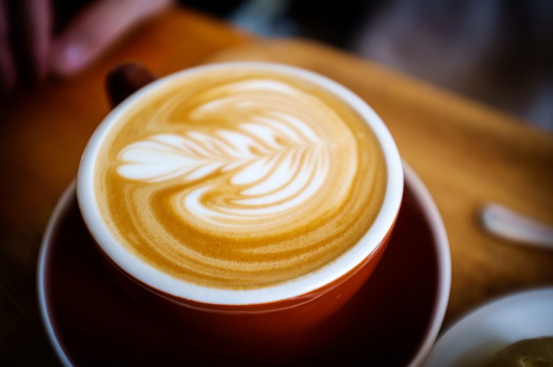 latte in a red cup on a saucer with leaf like foam art on a wooden table, red cappuccino 4k