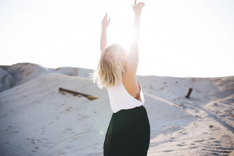 a blonde bowman lifting up her hands while standing on a sandy hill on a bright day, woman lifting up her hands 4k