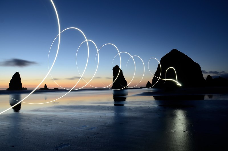 a light painting shot captured with long exposure in cannon beach, light painting spirals over the water 4k