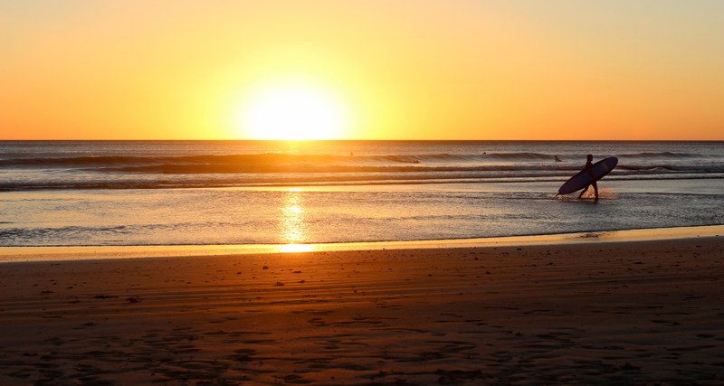 a surfer holding a surfboard walking in the ocean in san juan del sur, sundown on a day of surfing 4k