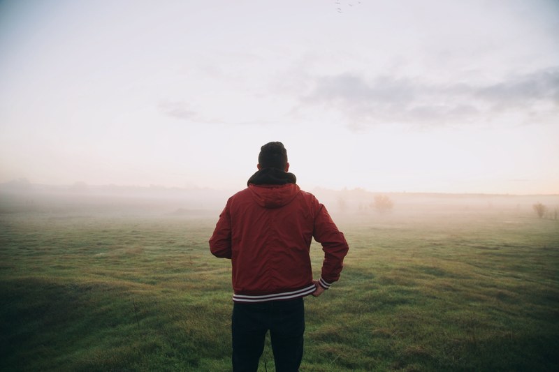 a man in a red jacket standing in a foggy green field, man in a foggy green field 4k
