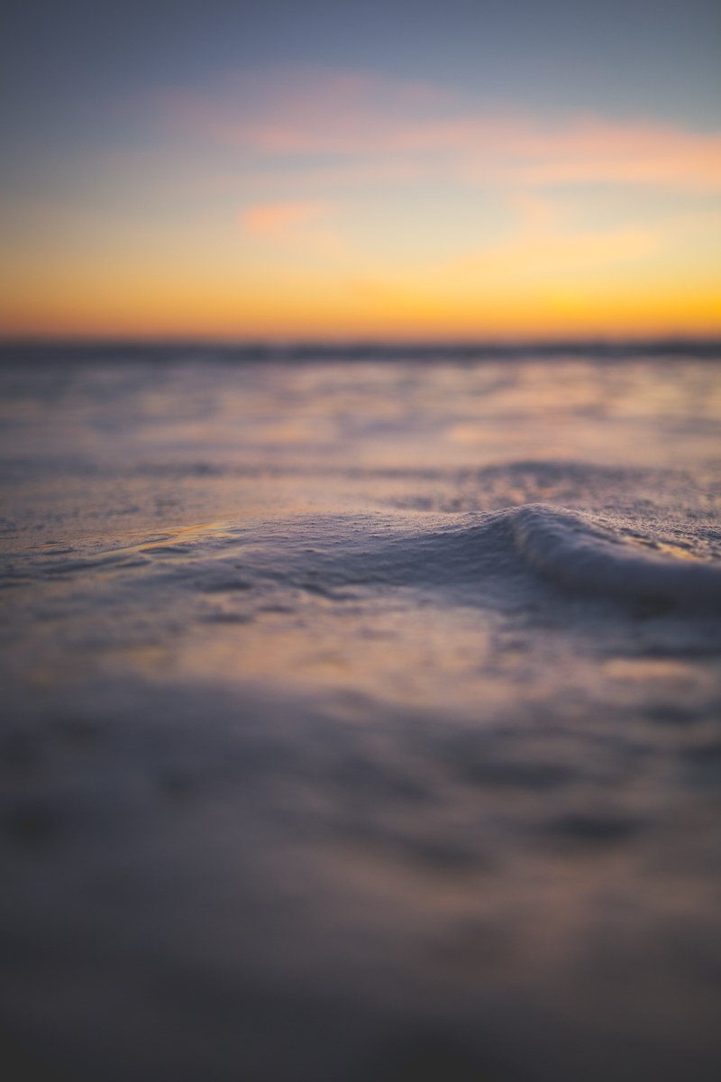 a portrait shot of a calm sea shimmering beneath a blue and orange sunset sky, sea reflecting the sunset 4k