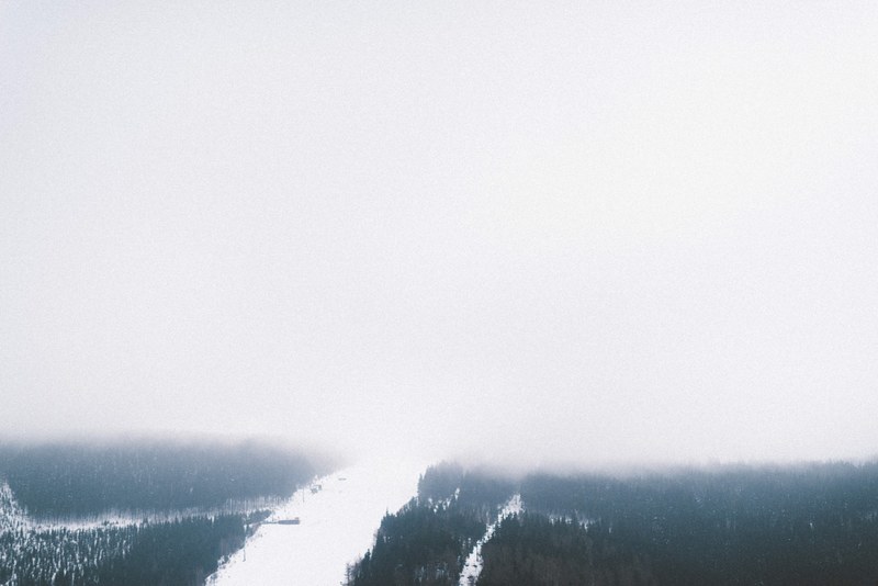 a high view of a snowy wooded slope shrouded in heavy mist in pindlerv mln, thick mist on a wooded slope 4k