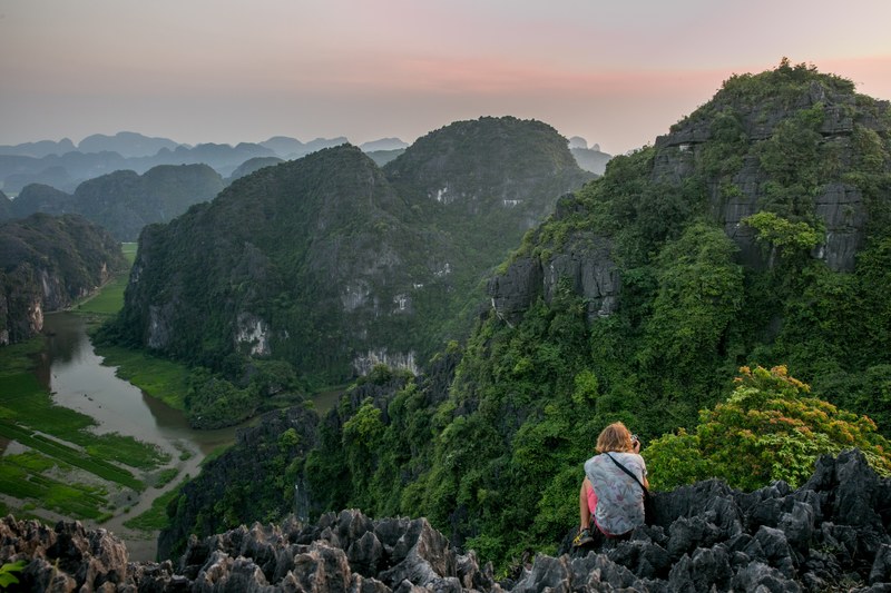 a person crouching on jagged rocks with a camera, lying dragon 4k