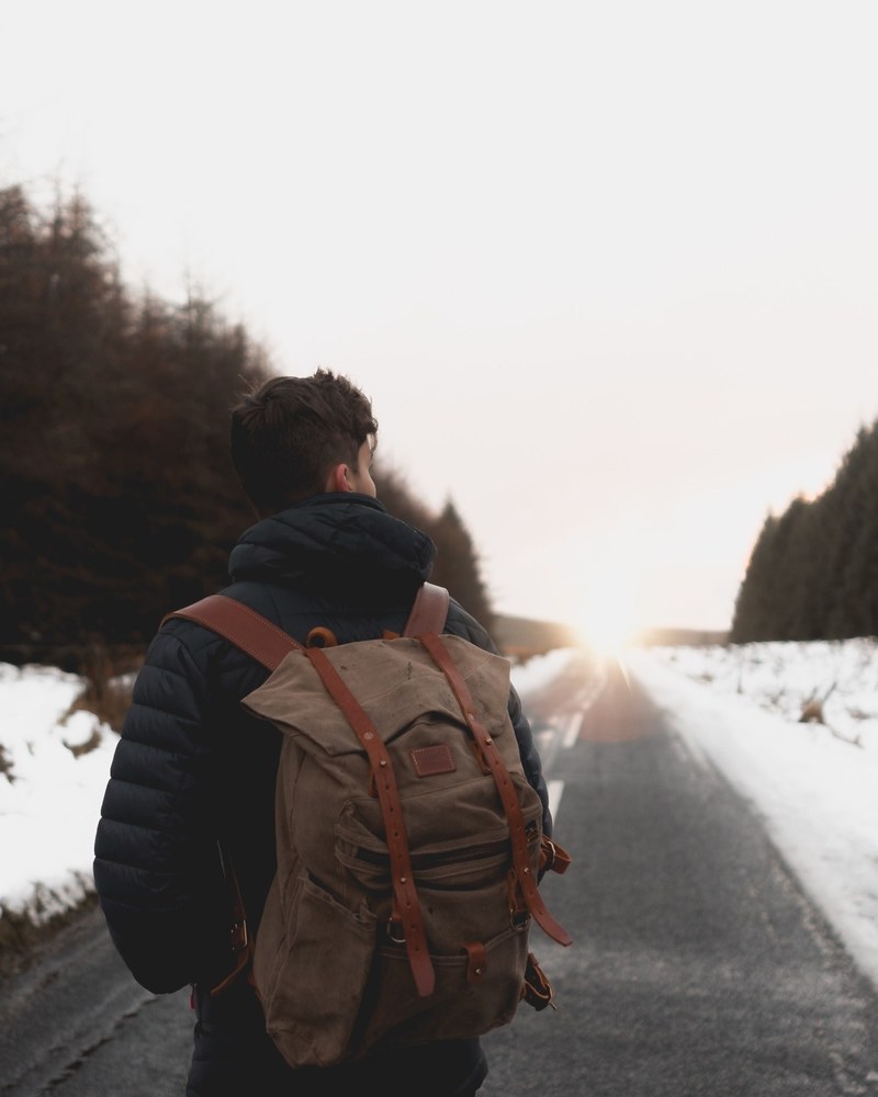 a guy walks with a backpack on a road during the winter in springwell forest united kingdom, explore 4k