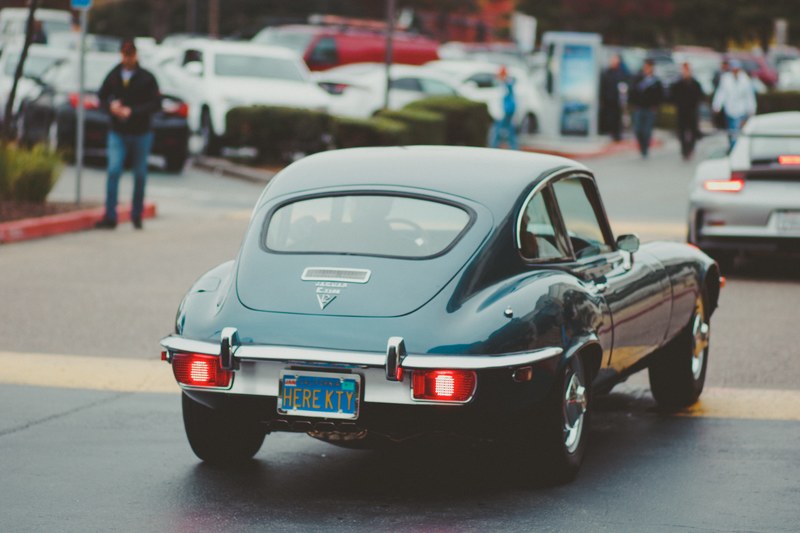 stylish luxury vintage green car driving on road with pedestrians walking nearby, luxury vintage green car 4k