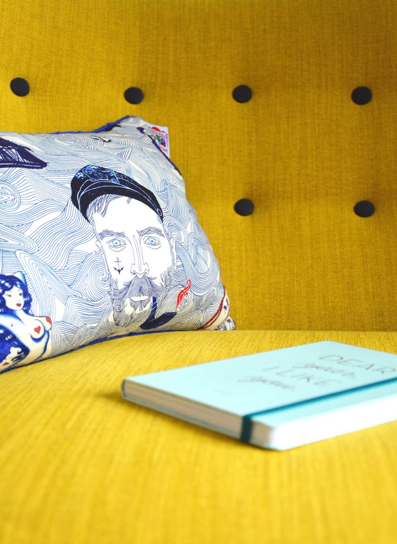 hardcover book sitting on the yellow couch in front of nautically themed pillow, hardcover book on a yellow couch 4k