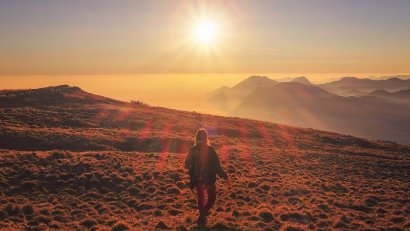 a woman walking on a mountain during sunrise or golden hour in monte altissimo di nago, monte altissimo di nago sun 4k