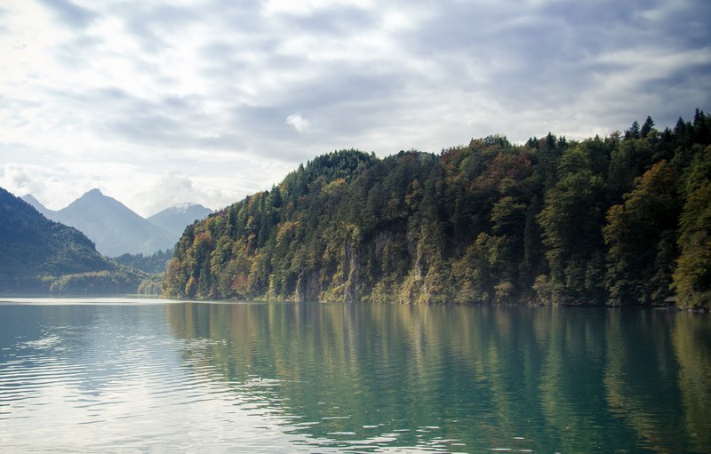 steep wooded cliffs over a calm lake with mountains on the horizon, forested cliff over the lake 4k