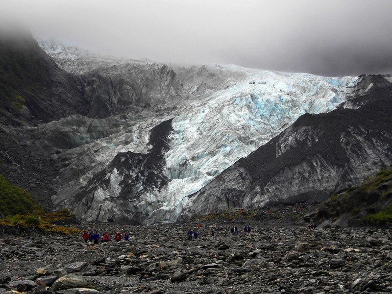 a group of mountaineers on a rocky slope at the foot of an ice blue mountain, climbing up the icy mountain 4k