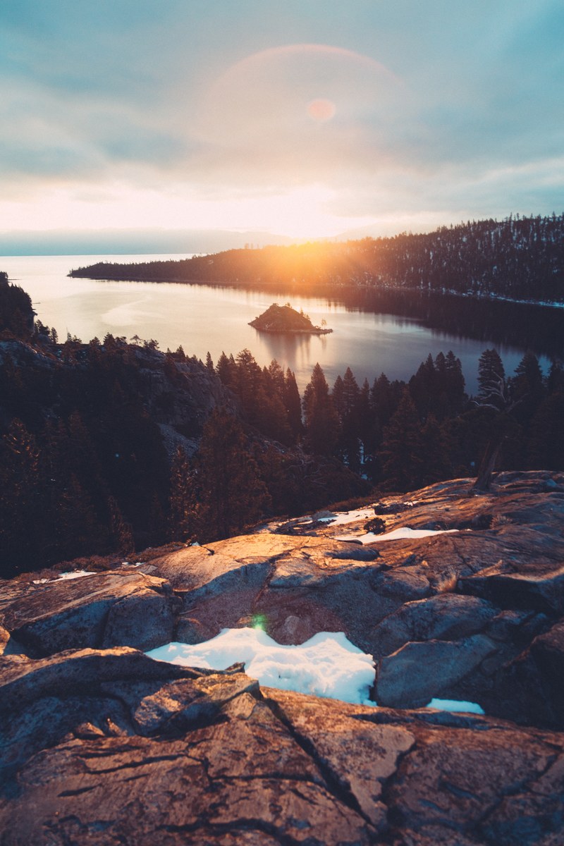 a beautiful landscape with smooth rocks in the foreground and a vast lake in the distance, sunrise over rocky lake shore 4k