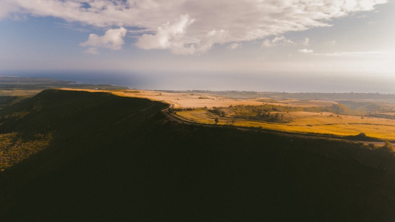 drone view of brown grassy valley dropping off into a cliff with a cloudy sky, hawaii road 4k