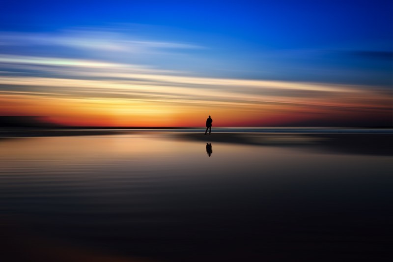 colorful sunset reflecting off the beach in tel aviv yafo with person standing in horizon, reflecting colorful beach sunset 4k