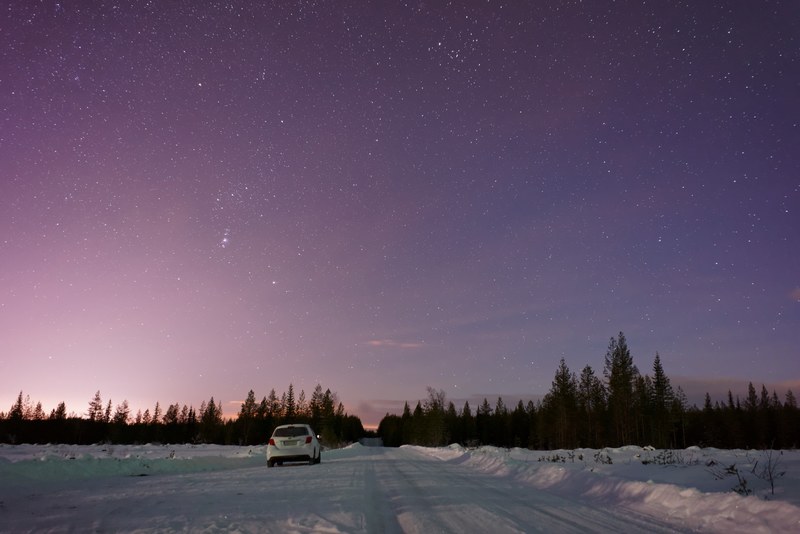a white hatchback parked on the side of a snowy road, chasing the northern lights 4k
