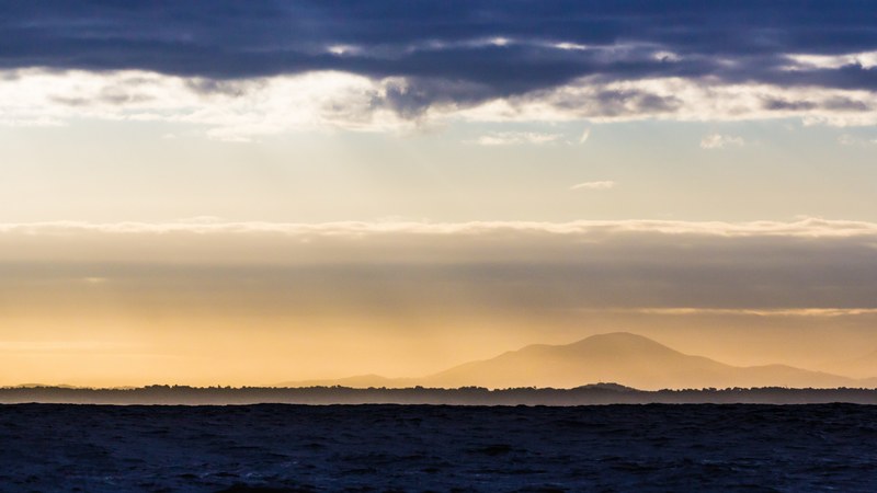 silhouette of a mountain seen from the surface of a choppy sea during sunset, sunset over capbreton shore 4k