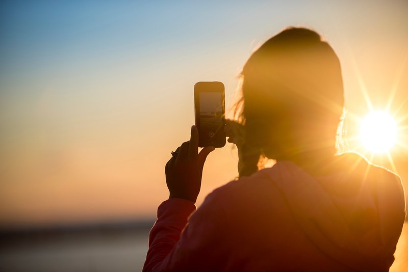 a woman on the beach taking a photo on her smartphone during golden hour, woman shooting ocean sunset 4k