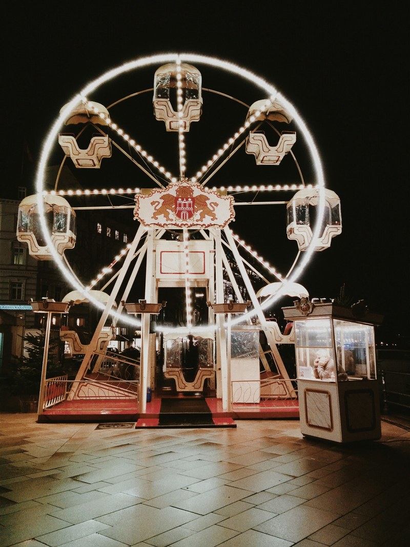 small ferris wheel lit by bulbs at night with a person waiting in a booth, ferris wheel at night 4k