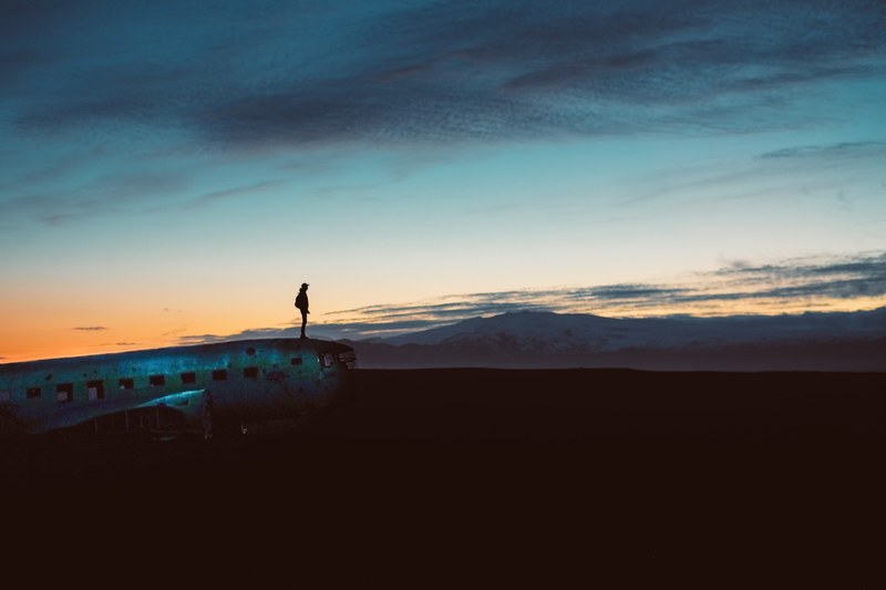 silhouette of a person wearing hat standing at edge of aircraft during a cloudy sunset, man standing plane sunset 4k
