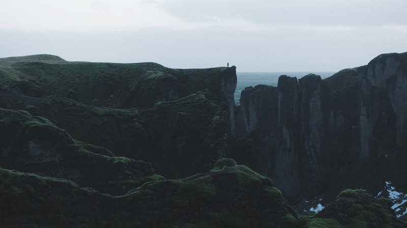 a distant shot of a lone silhouette standing on the edge of a rocky cliff, on the edge of a cliff 4k