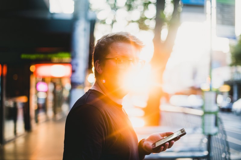 a person in glasses holding an iphone with their face obscured by bright sun in melbourne, a melbourne sunset 4k