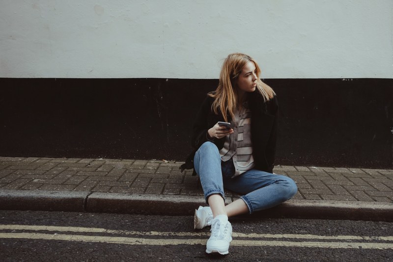 a blonde woman wearing a black jacket sitting on the curb in marylebone, where to next 4k