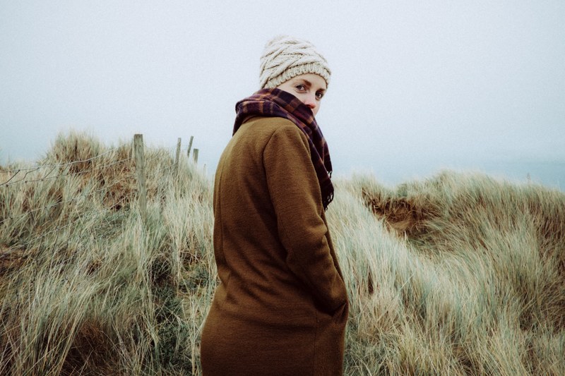 a woman in a knit cap and sweater turns toward the camera among coastal dunes, woman with coastal dunes 4k