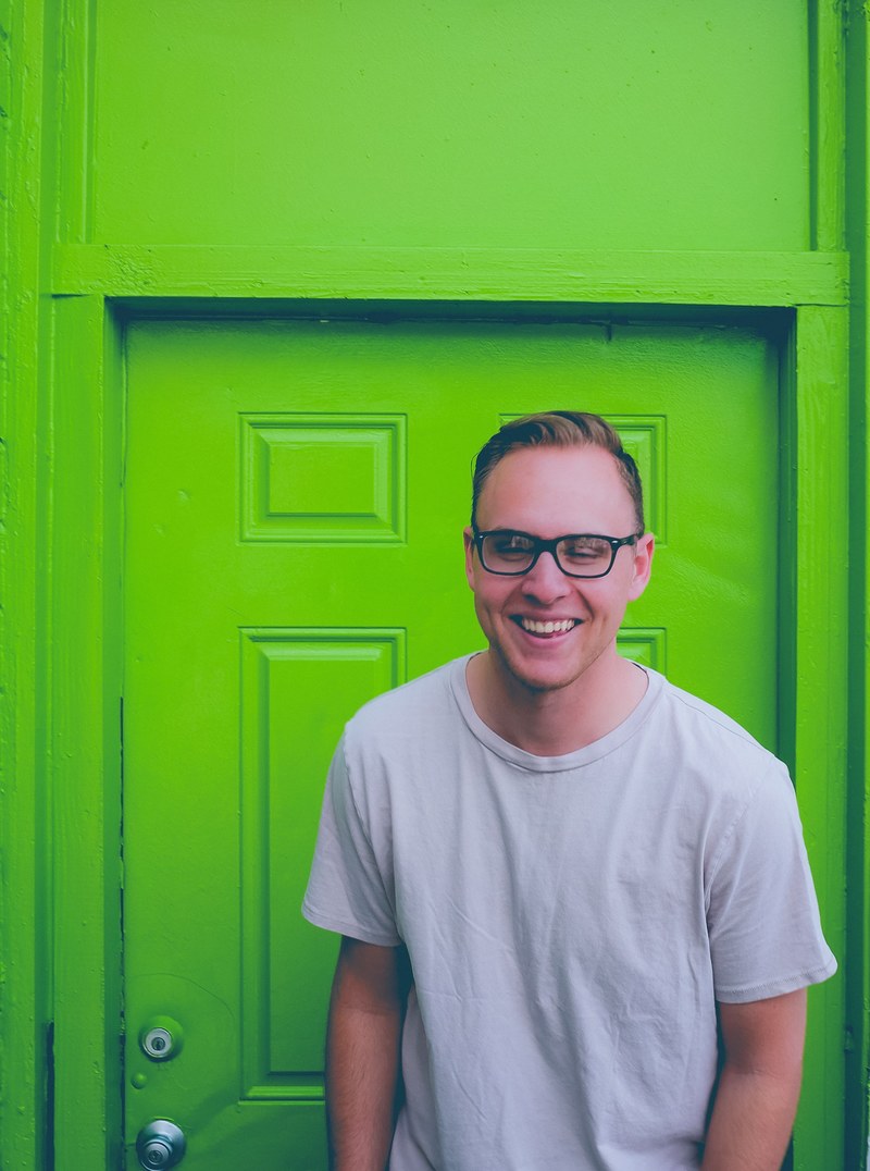 a man wearing glasses smiling while standing in front of a green door, _man in front of green door 4k