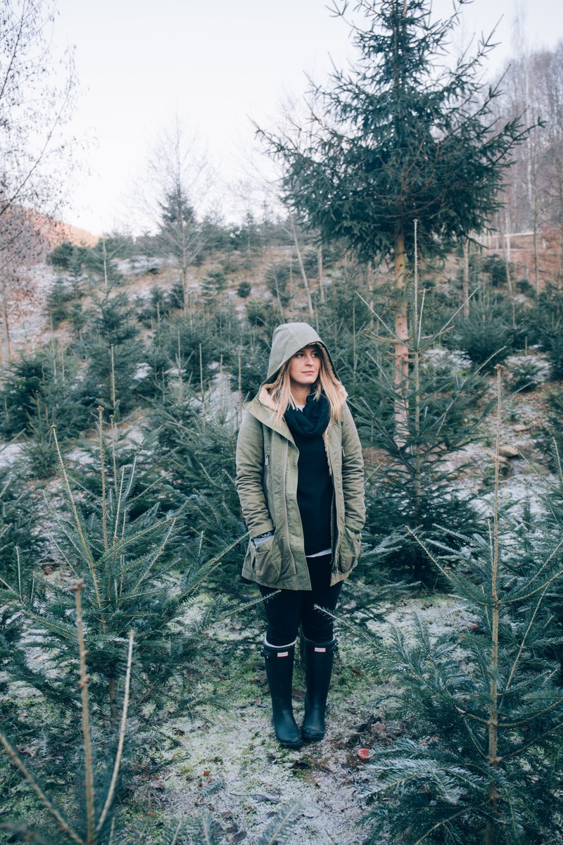 a woman wearing a coat and hood in the snowy forest in romania, woman among spruce trees 4k