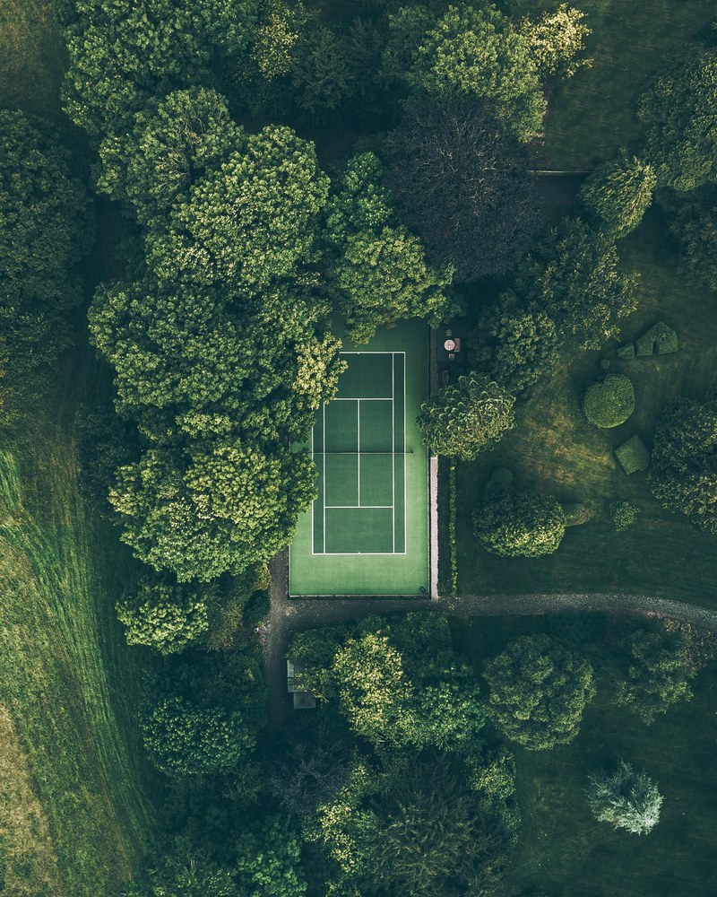 a drone shot of a green tennis court surrounded by trees in frampton england, lost in the wilderness 4k