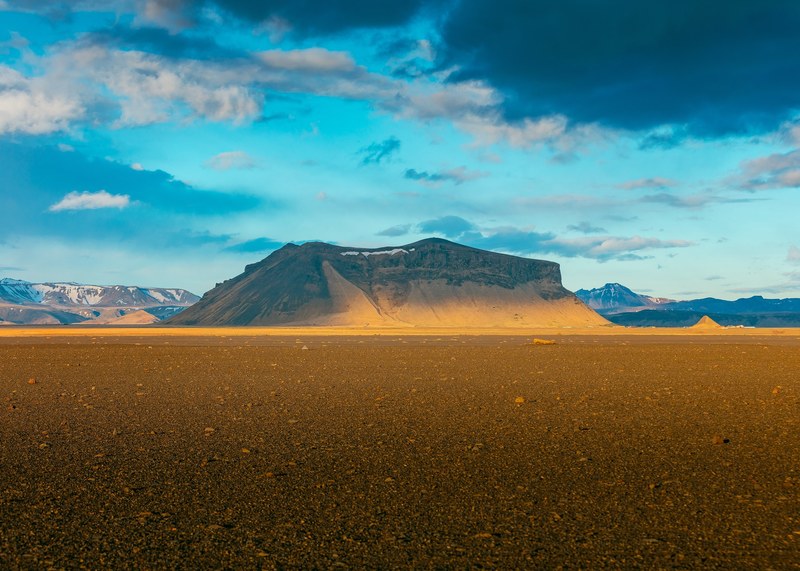 a rocky plain with a flat mountain at the back on a cloudy day, break in the clouds 4k